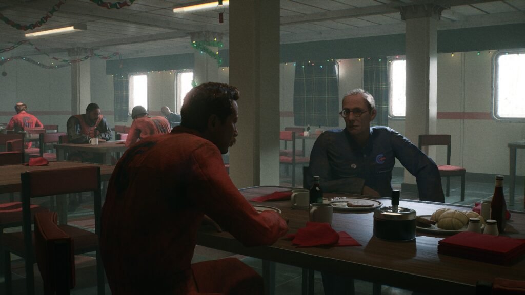 a canteen on an oil rig, men sit in the background eating, the foreground shoes two men sitting on a table talking with empty plates of food and coffee mugs.  