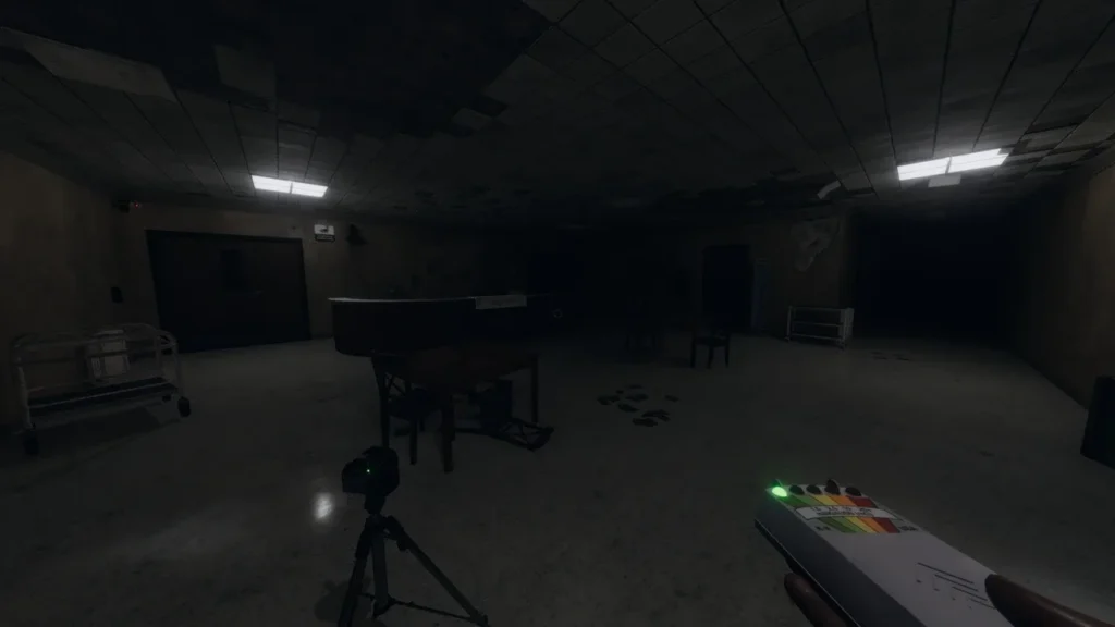 a large room with a piano inside in phasmophobia. some fluorescent lights are on in the celling and the players hand in the bottom right of the screen is holding an EMF with one light illuminated. a camera on a tripod sits in front of the player facing into the waide room.